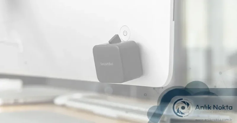 SwitchBot'un şarj edilebilir buton itici cihazı, bir monitörün butonuna takılı halde gösteriliyor.