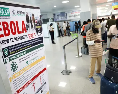 Nijerya'da Ebola farkındalık bannerı önünde duran yolcular